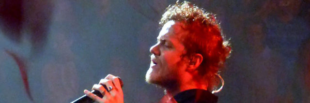 Dan Reynolds sings onstage while wearing a blue or black outfit
