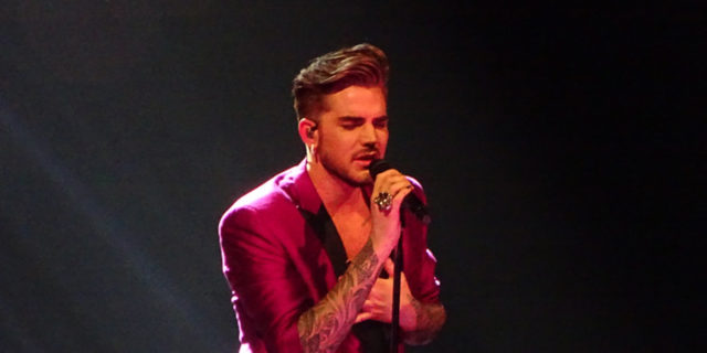 Adam Lambert performs onstage while wearing a purple suit.