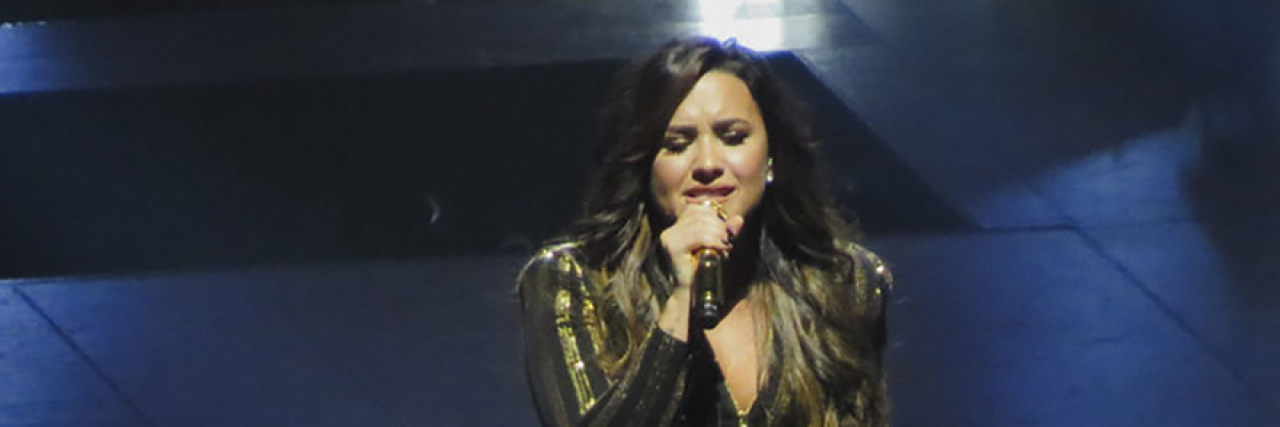 Demi Lovato singing onstage while wearing a black and gold costume
