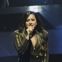 Demi Lovato singing onstage while wearing a black and gold costume