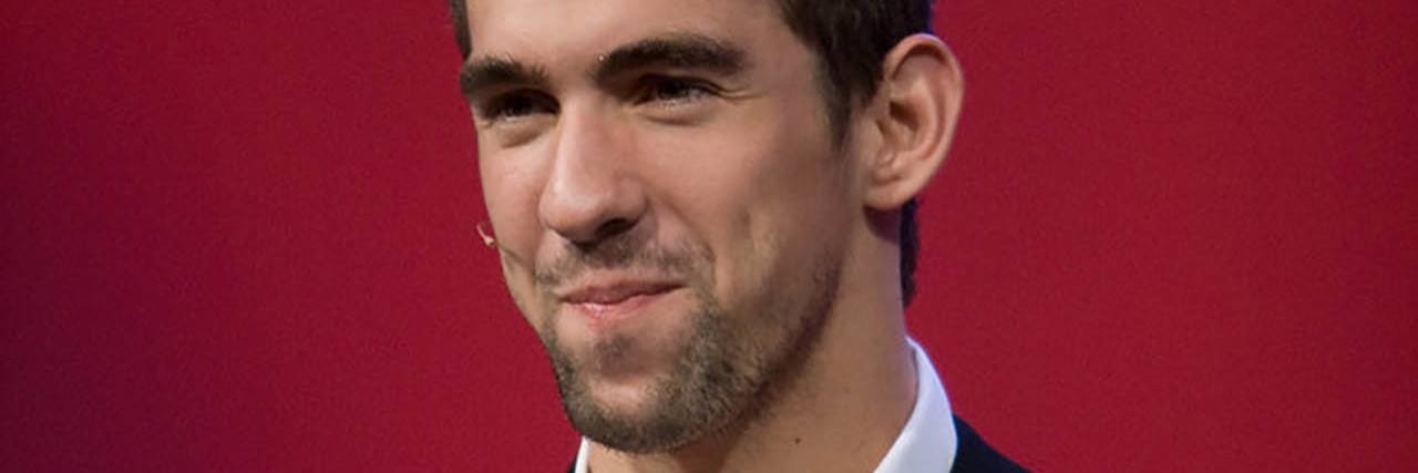 Michael Phelps poses in front of a red wall in a suit