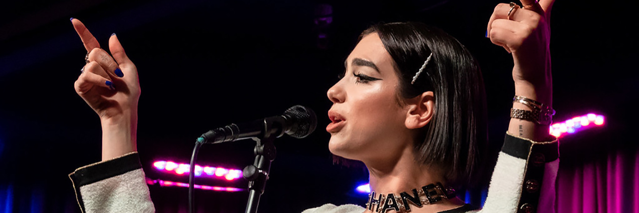 Dua Lipa Criticizes United Airlines for Peanut Allergy Treatment Dua Lupia points at the crowd while singing onstage.