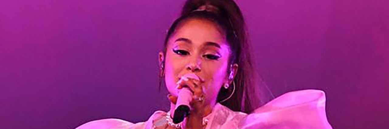Ariana Grande sits down while singing onstage at a concert