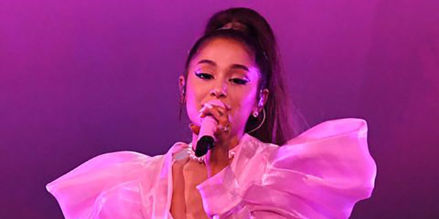 Ariana Grande sits down while singing onstage at a concert