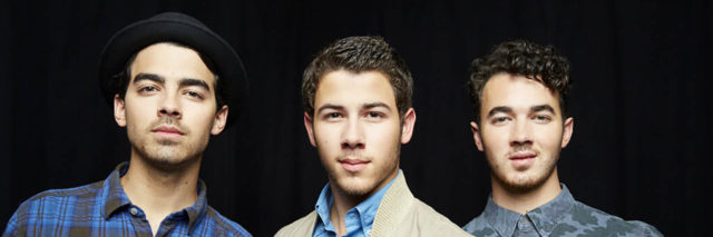 The Jonas Brothers pose together, wearing outfits with blue in them