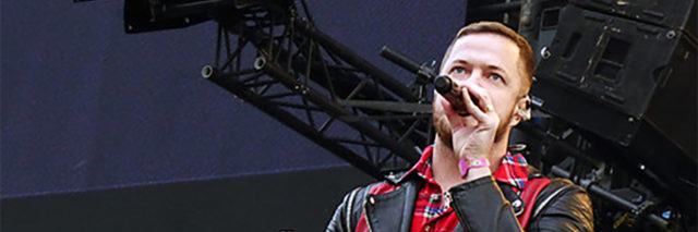 Dan Reynolds sings onstage while wearing a black and red outfit