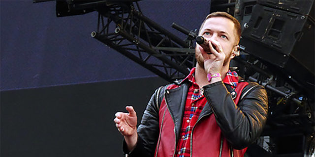 Dan Reynolds sings onstage while wearing a black and red outfit