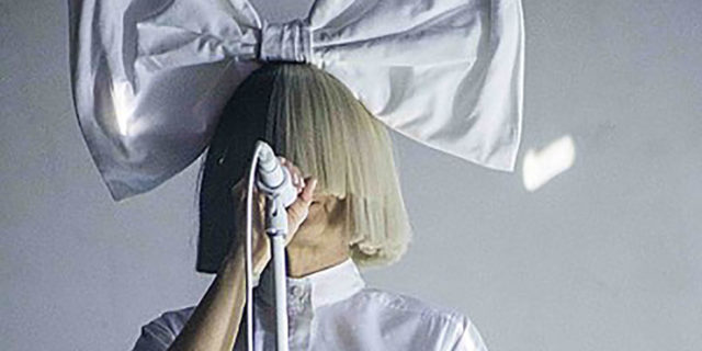 Sia singing onstage with a giant bow on her head