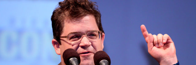Patton Oswalt speaks from a podium at an event