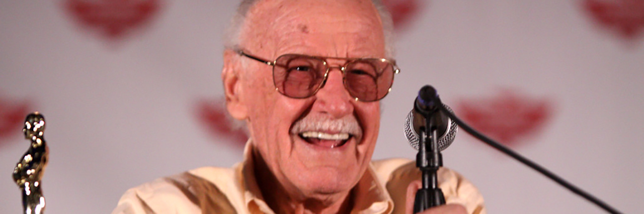 Stan Lee smiles while accepting an award and giving a speech at an event