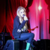 Avril Lavigne sings while sitting down in a black ensemble