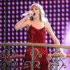 Taylor Swift performs onstage while wearing a red dress