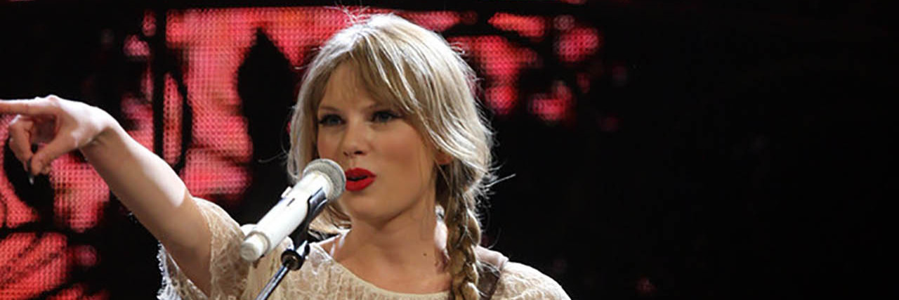 Taylor Swift performs onstage while wearing a white dress