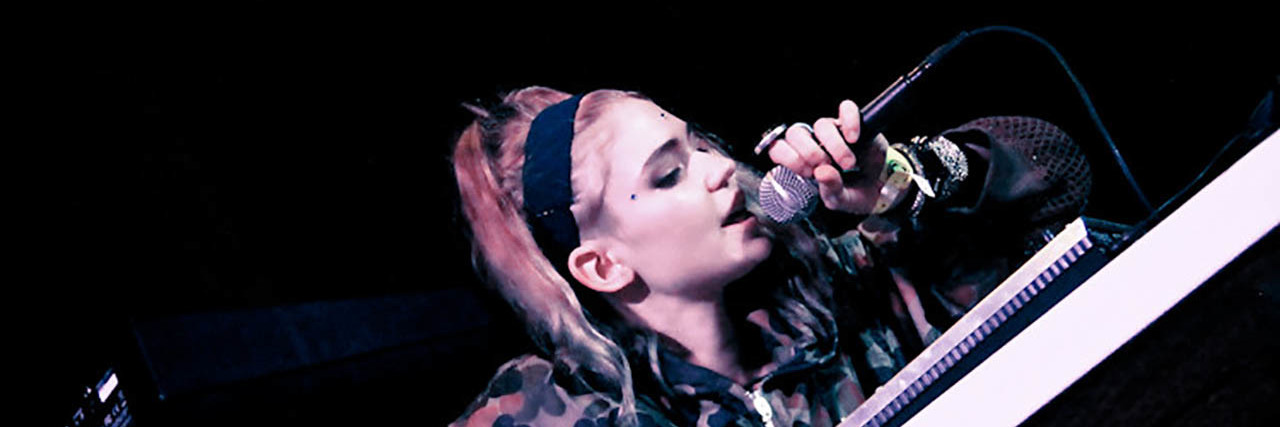 Grimes sings onstage while wearing an outfit with patterns on it.