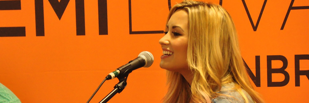 A side shot of Demi Lovato, who is talking into the microphone while wearing a denim jacket