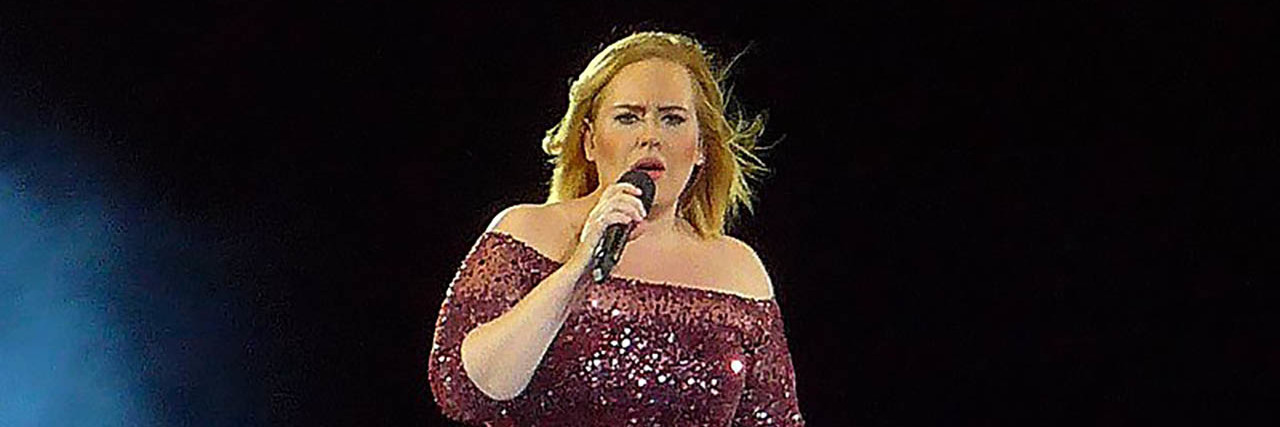 Adele performs onstage while wearing a purple gown