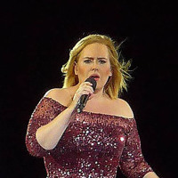 Adele performs onstage while wearing a purple gown