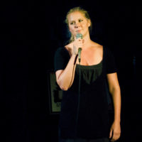 Amy Schumer in a black dress talking onstage