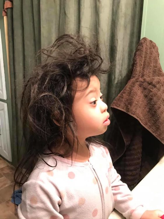 Young girl with Down syndrome looking at knotted hair in the mirror