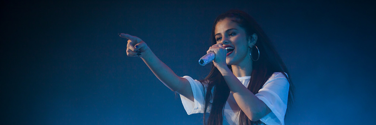 Selena Gomez singing onstage while wearing a white costume