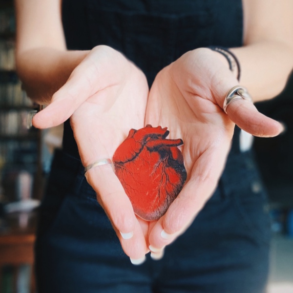 A woman holding out a small anatomical heart in her hand.
