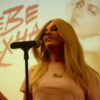 A close-up of Bebe Rexha singing in front of her name