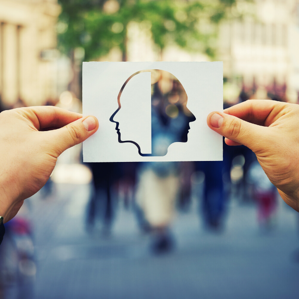 Man holding image of two profiles of faces. One profile is cut out and the other is white. Through the cut out profile you can see the hustle and bustle of a city in the background.