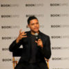 Trevor Noah wearing a black outfit and speaking at a BookExpo event