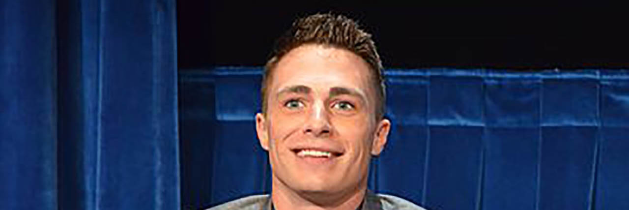 Colton Haynes sits in a chair while at a panel