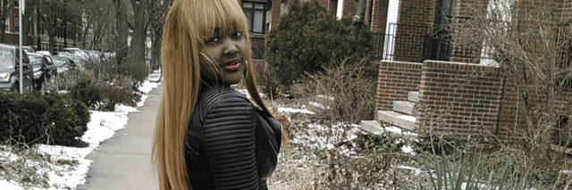 CupcakKe poses on a sidewalk and wears a black top and plaid pants