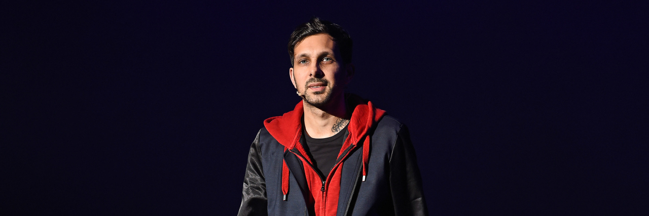 The magician Dynamo stands onstage while wearing a black, blue and red outfit.