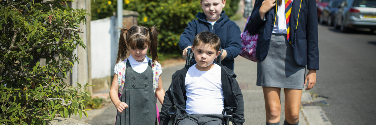 Teaching Typical Kids How to Interact With Peers With Disabilities Child in wheelchair with siblings and friends going to school.