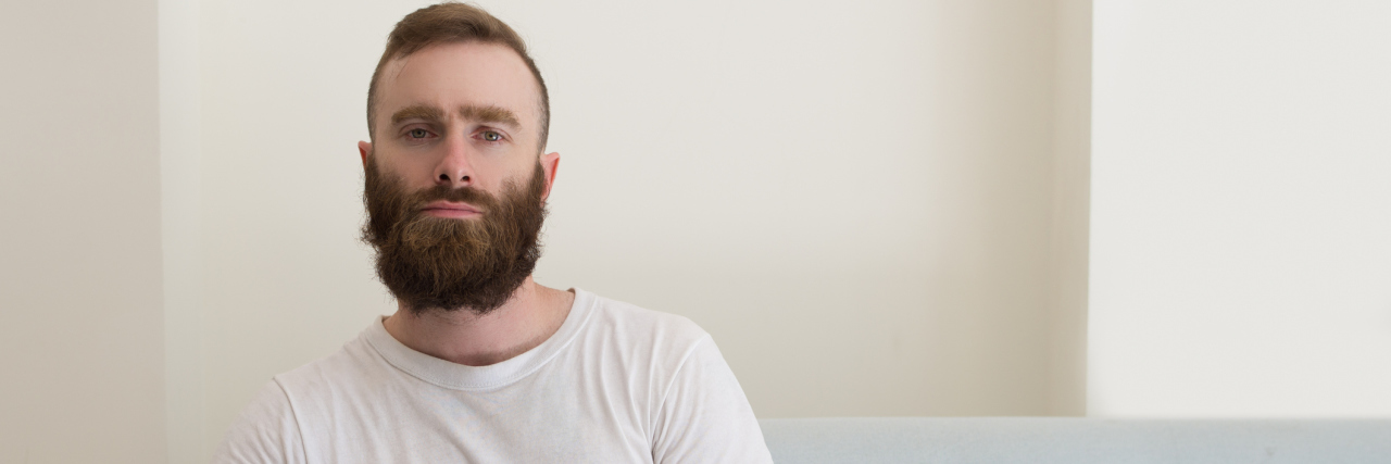 man with a beard sitting on the couch staring seriously straight ahead