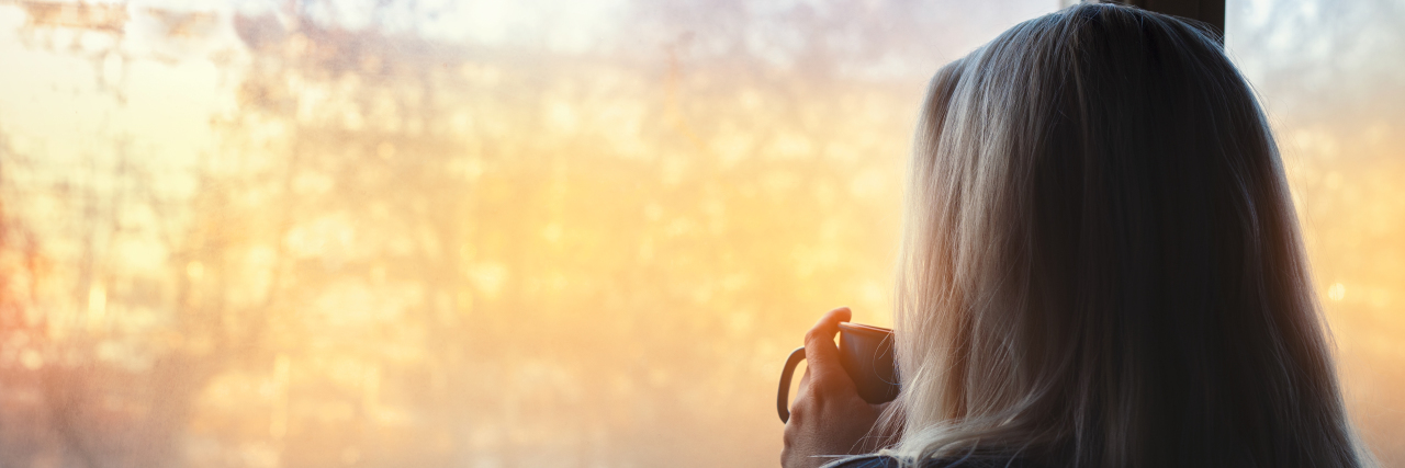 Self-Isolation Due to COVID-19 as Someone With Dwarfism Woman standing by the window, with coffee cup.