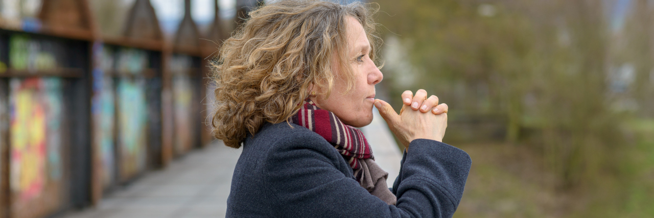 The Coronavirus Is Causing People to Finally Value The Chronically Ill woman standing outside on a bridge looking out thoughtfully