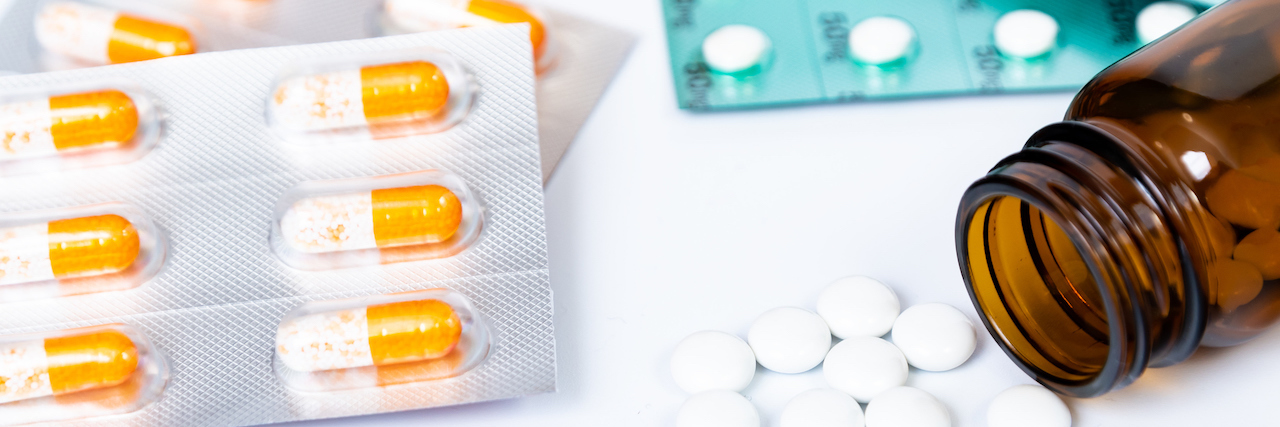 What to Do If You Can't Afford Your Medications During COVID-19 Several medications, including a bottle of spilled white pills, capsules and tablets on a white background