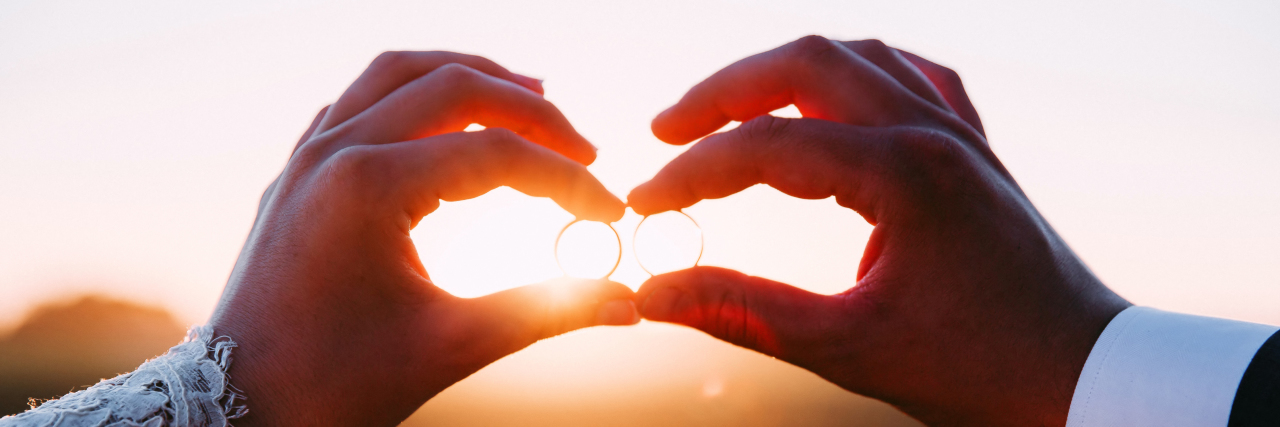 How We Adapted Our Wedding for My Disabilities Two married people holding wedding rings at sunset.