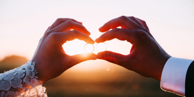 How We Adapted Our Wedding for My Disabilities Two married people holding wedding rings at sunset.