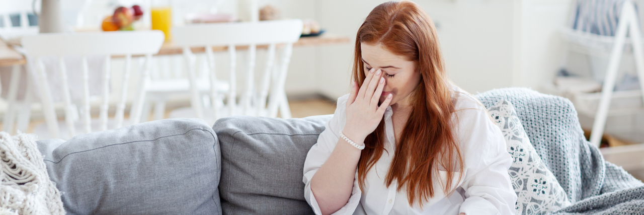 5 Tips for Managing Borderline Personality Disorder During COVID-19 red-haired woman sitting on the couch with a hand on her forehead, exhausted