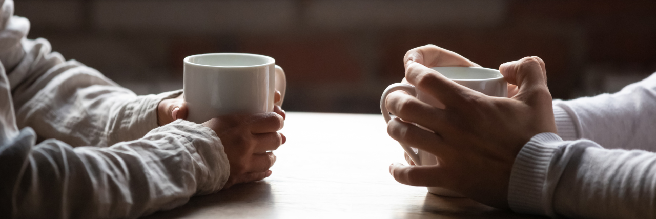 How Autistic People Communicate Differently Woman and man sitting in cafe holding warm cups of coffee.