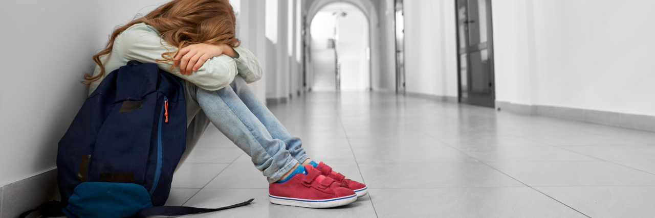 The Emotional Impact of GHD on Kids and Families photo of sad school girl sitting on floor in corridor with her face hidden in her arms