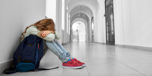 photo of sad school girl sitting on floor in corridor with her face hidden in her arms