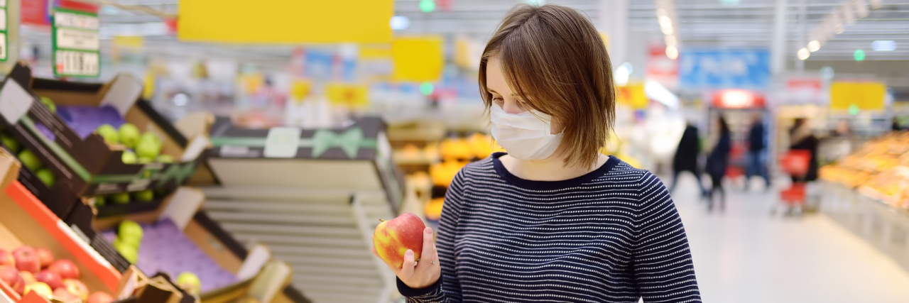 Woman wearing disposable mask shopping in supermarket during coronavirus pandemic.