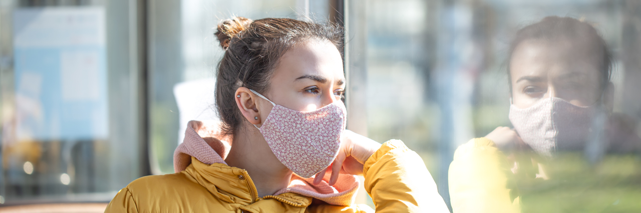 When I Was Judged for Wearing a Mask Before COVID-19 Young woman wearing a mask looking out a window.