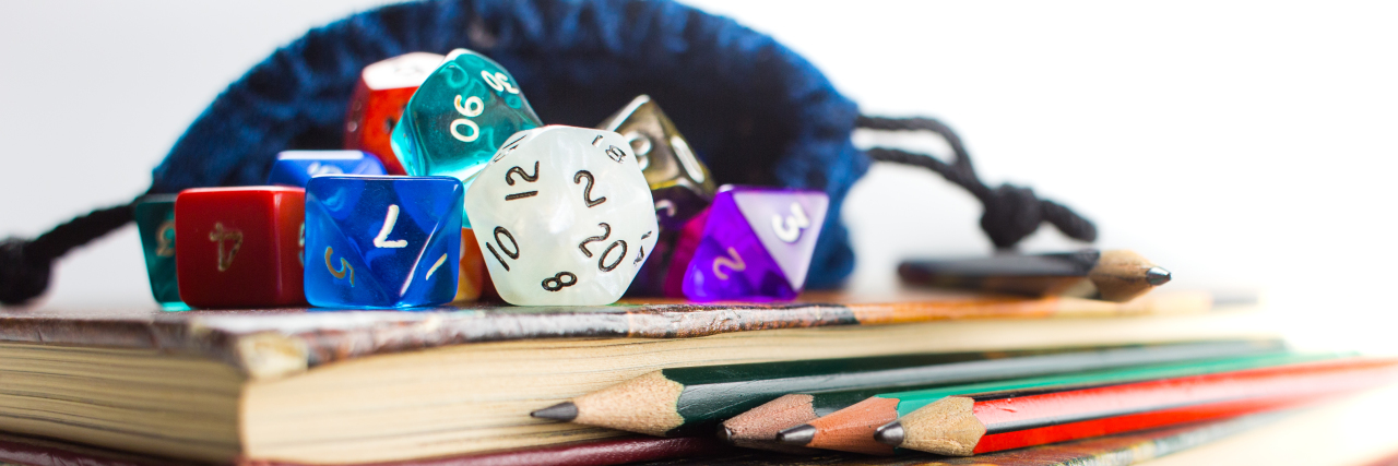 Multicolored dice with dice bag and pencils on top of three books.
