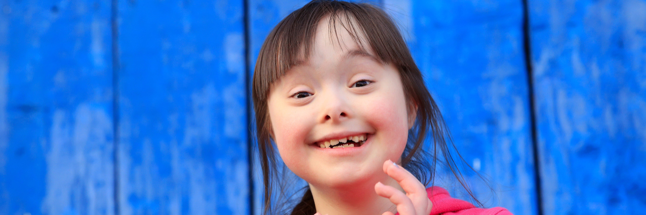 Young girl with Down syndrome smiling on background of the blue wall