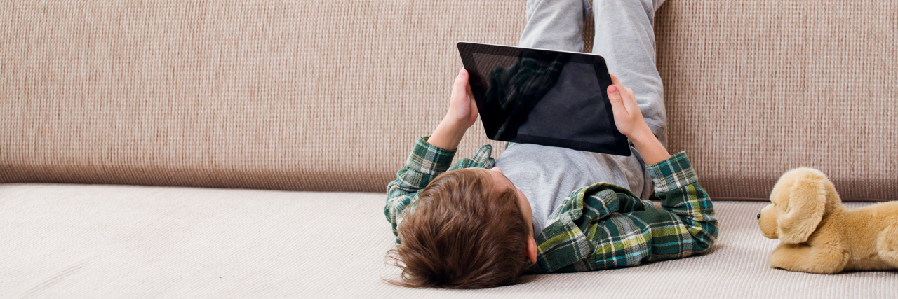 Boy playing with tablet on sofa.