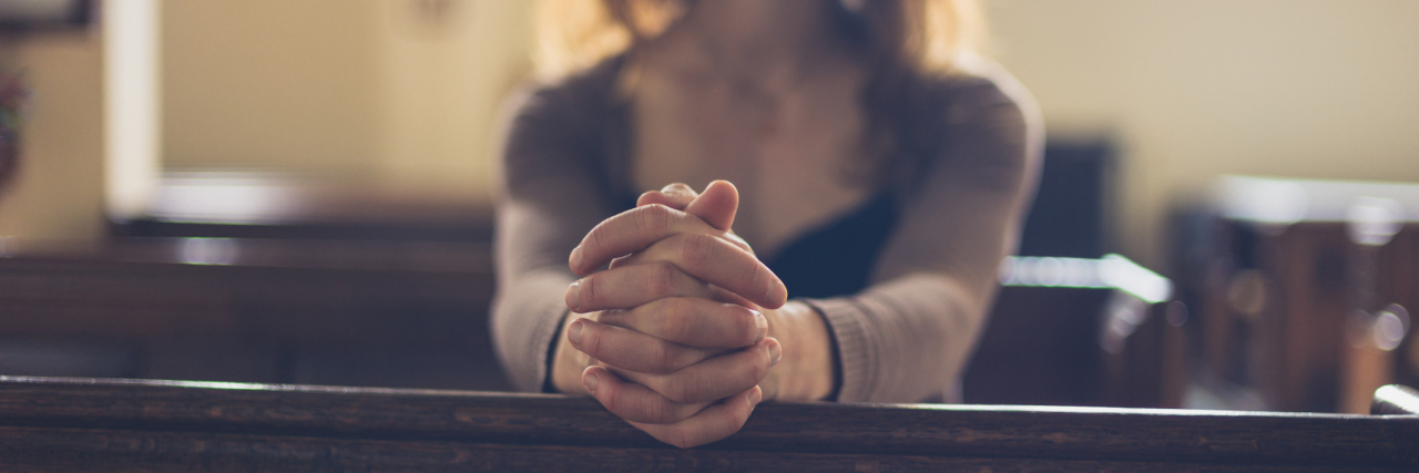 woman sitting at church alone with her hands folded in prayer