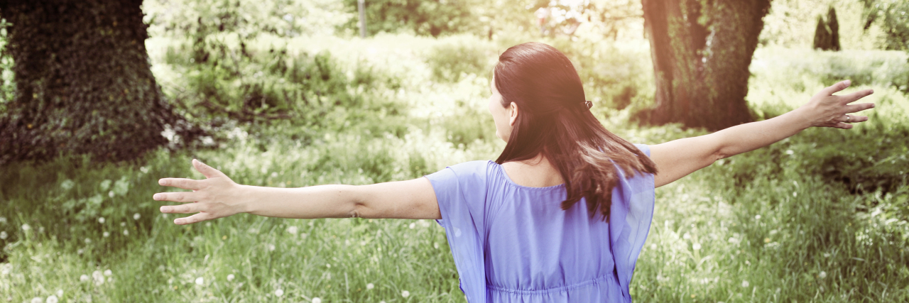 Let Autistic People Stim! Woman waving her arms outdoors.