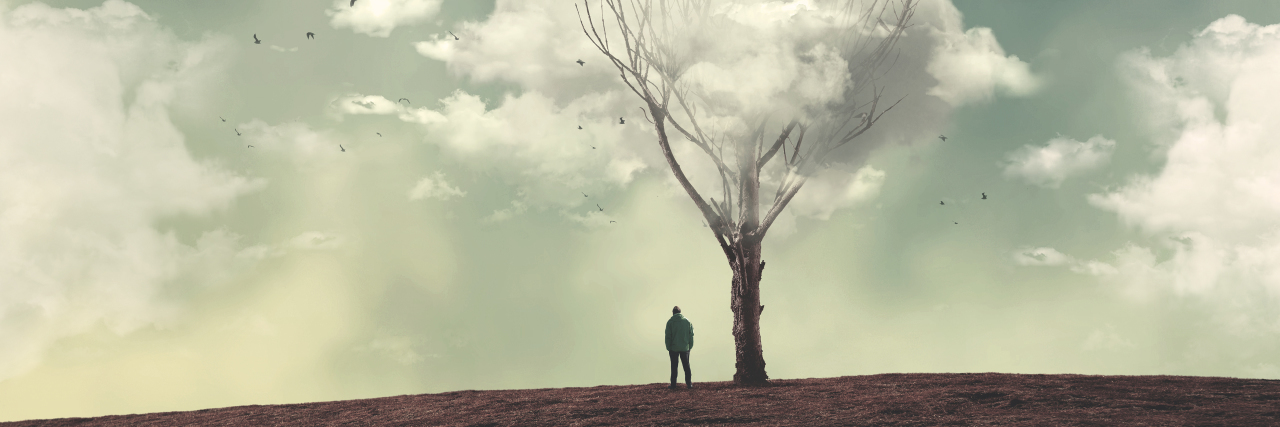 Man standing near bare tree with clouds overhead.